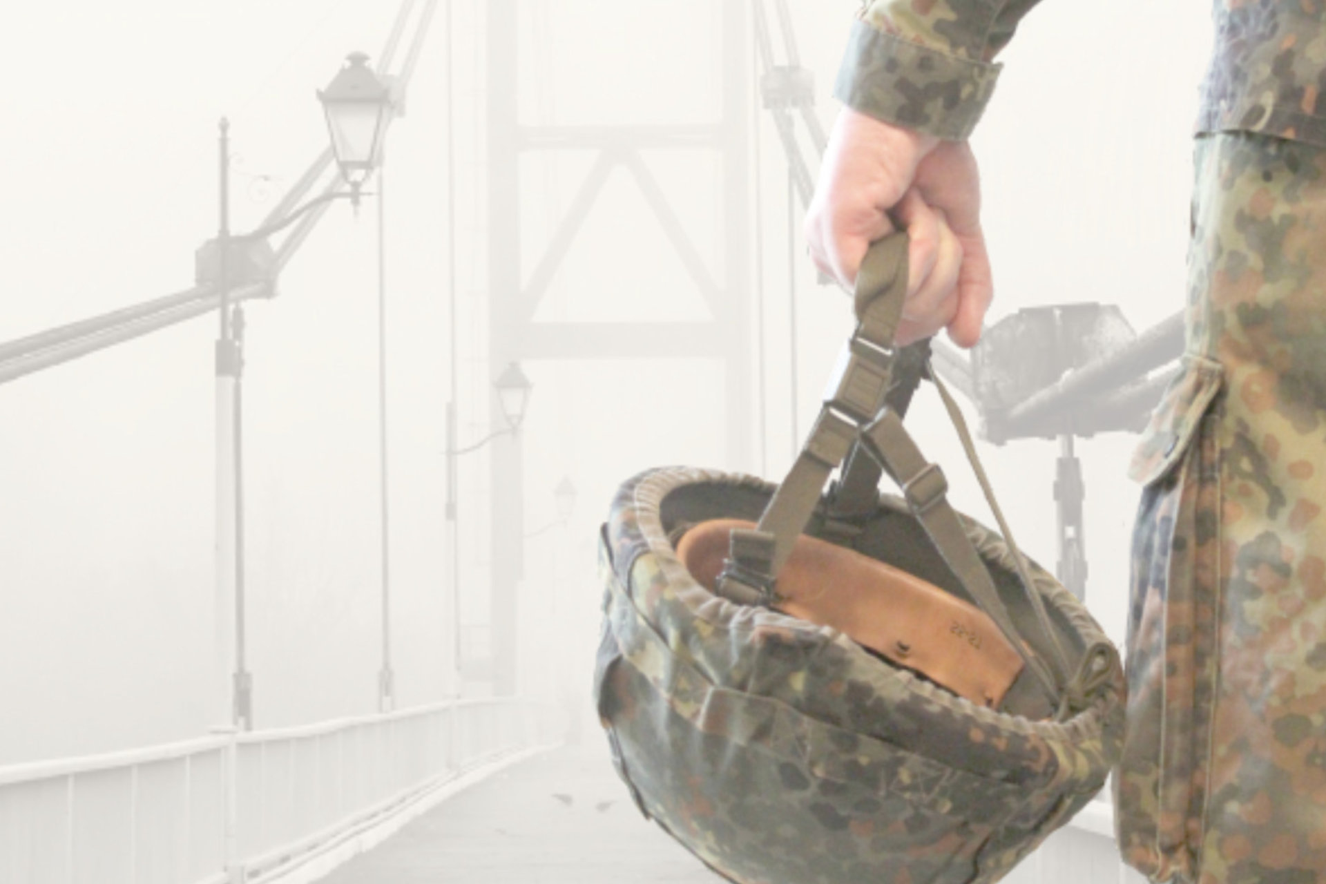Ein Soldat steht auf einer Brücke, die im Nebel verschwindet. Von dem Soldaten sieht man nur einen Teil seines Kürpers sowie seinen Helm, den er in der Hand haltend herabbaumeln lässt.