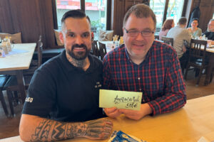 Auf dem Foto sieht man den Kameraden Maximilian Gronwald vom Team Tactical Raz links an einem Tisch sitzen. Er überreicht dem rechts von ihm sitzenden Vorsitzenden des Vereins Angriff auf die Seele e. V., Frank Eggen, ein symbolisches Papier des Spendenbetrages.