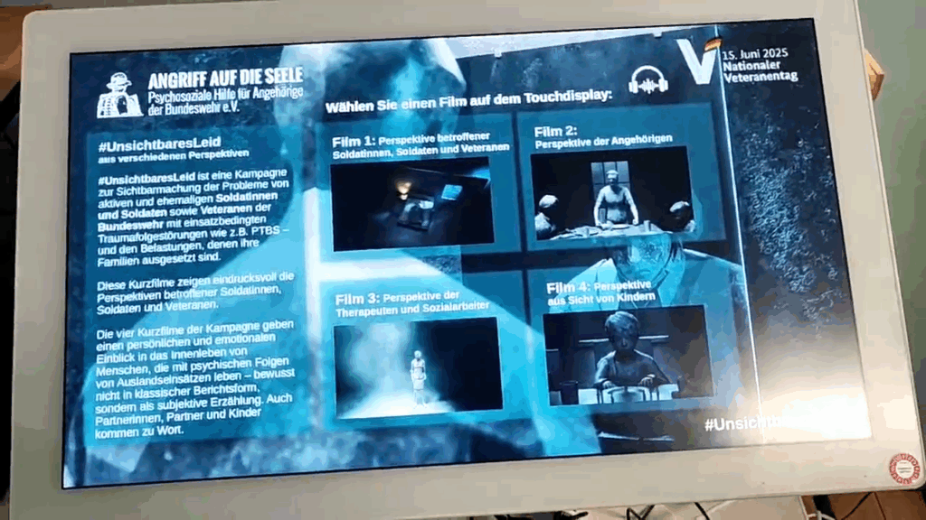 Blick auf das Touch-Terminal. Das Display zeigt die in blau gehaltene Oberfläche, auf der man sich die Filme der Kampagne #UnsichtbaresLeid auswählen und anschauen kann.